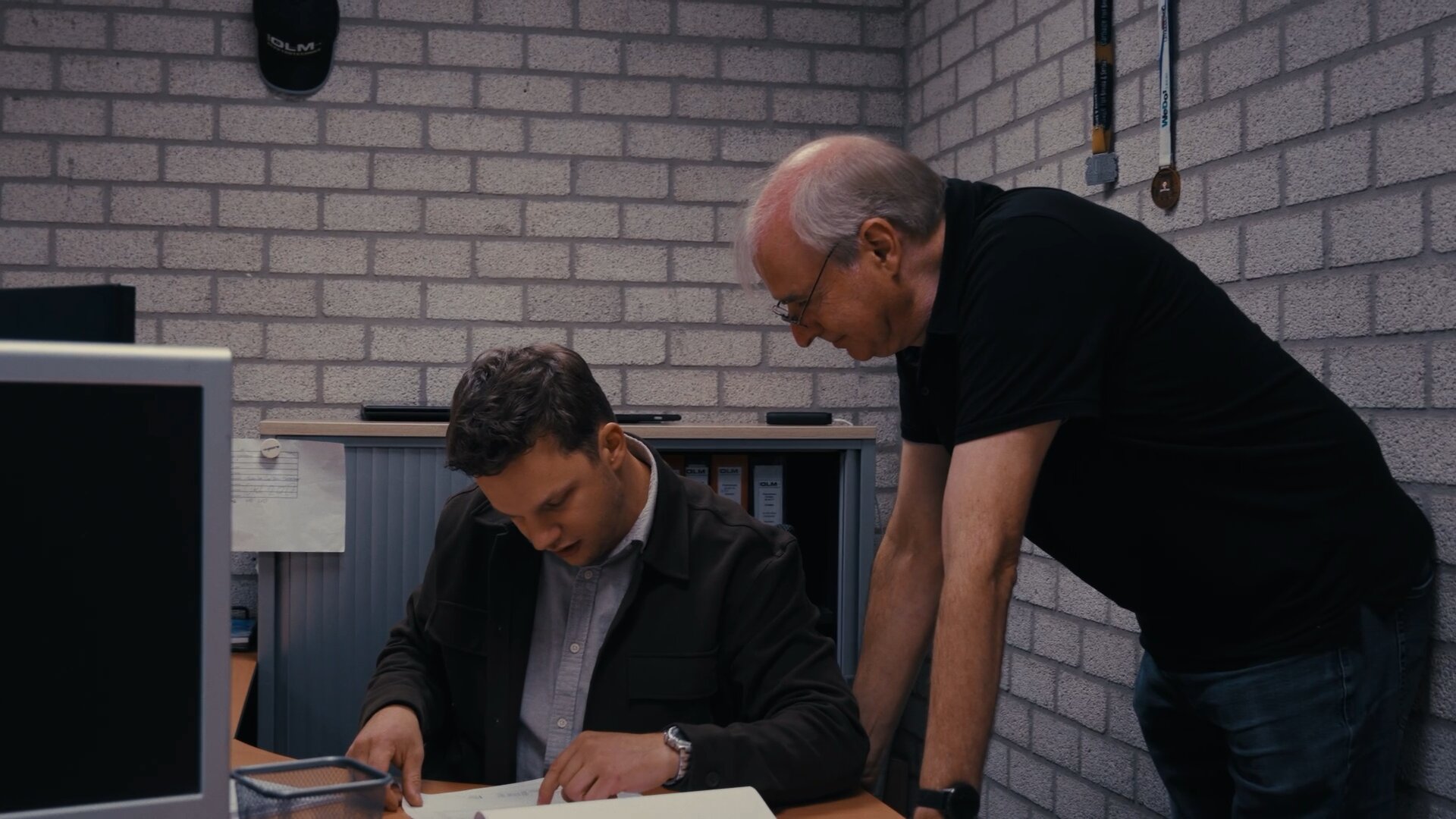 Medewerker leest een tekening door terwijl een collega over het bureau meekijkt.