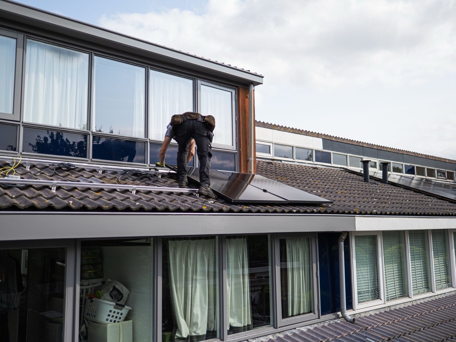 Monteur legt zwarte zonnepanelen op montagerails op het pannendak van een rijtjeswoning.