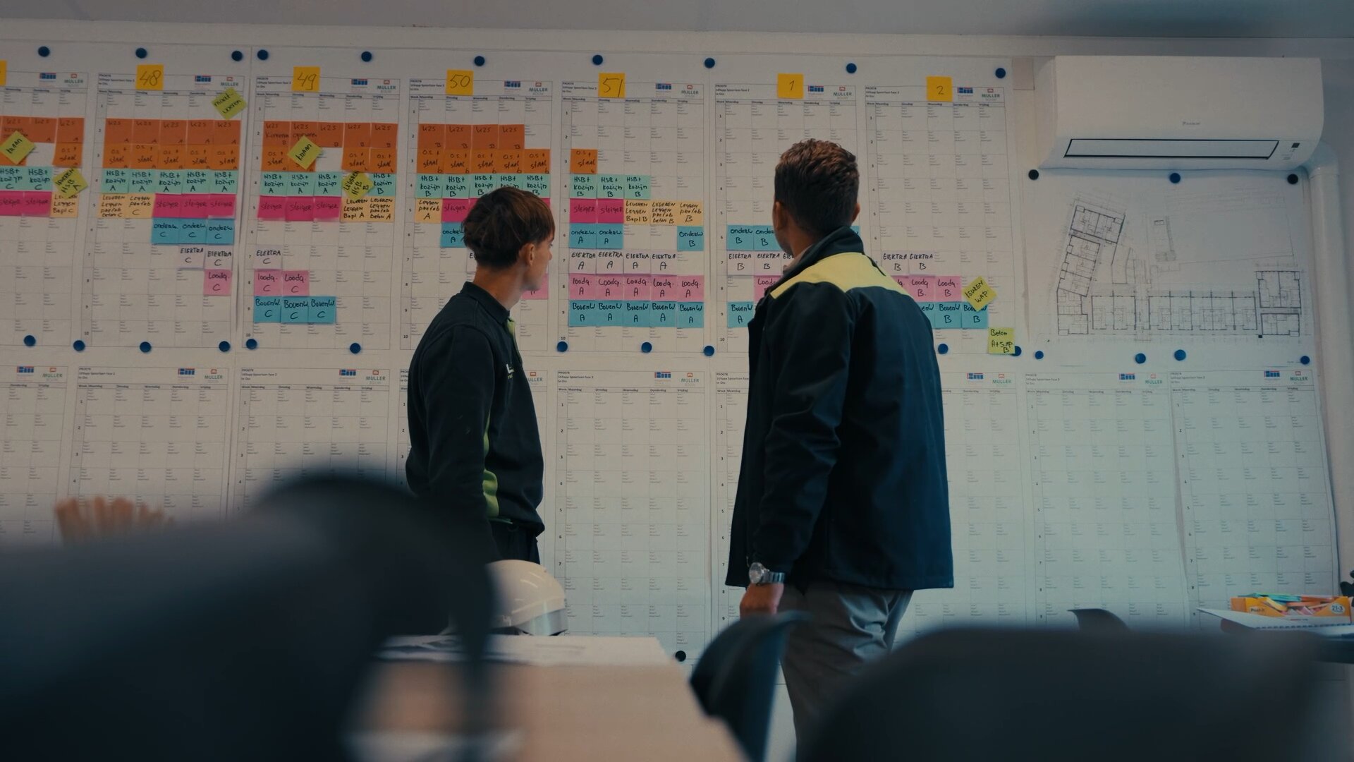 Jonge monteur en een collega lopen samen de weekplanning op het planbord door.