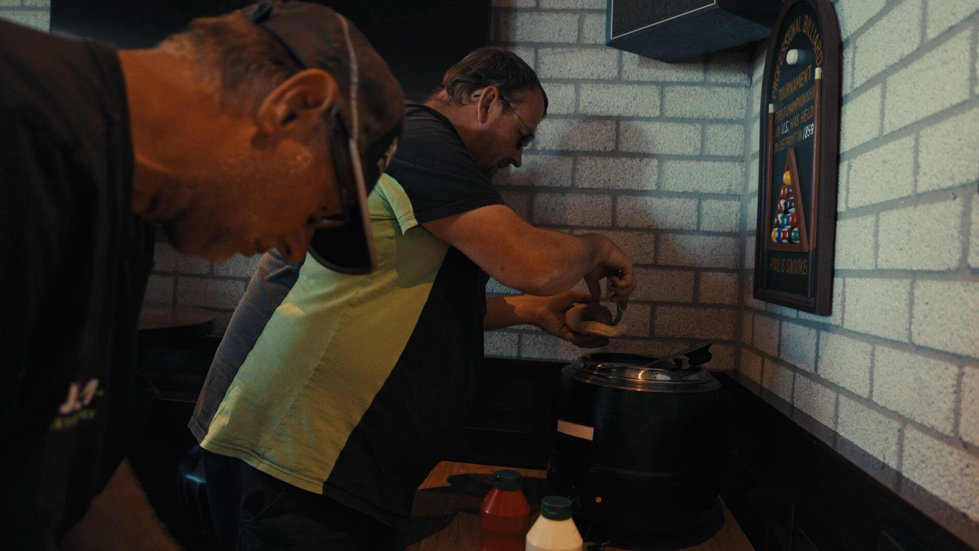 Collega's pakken een warm broodje uit de warmhoudpan in de kantine, met sauzen ernaast.